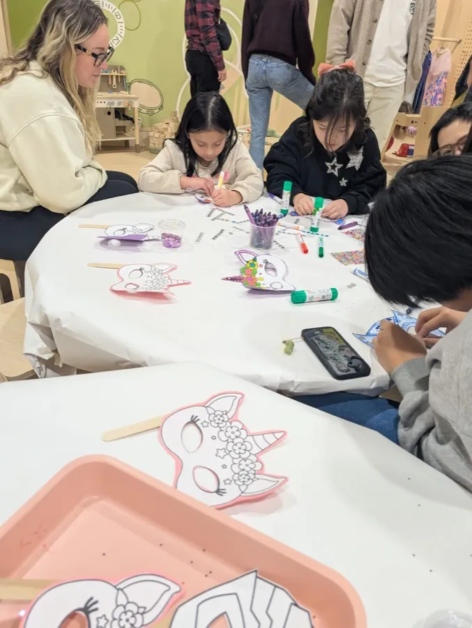 Littles and their parents decorating masks together around a long craft table